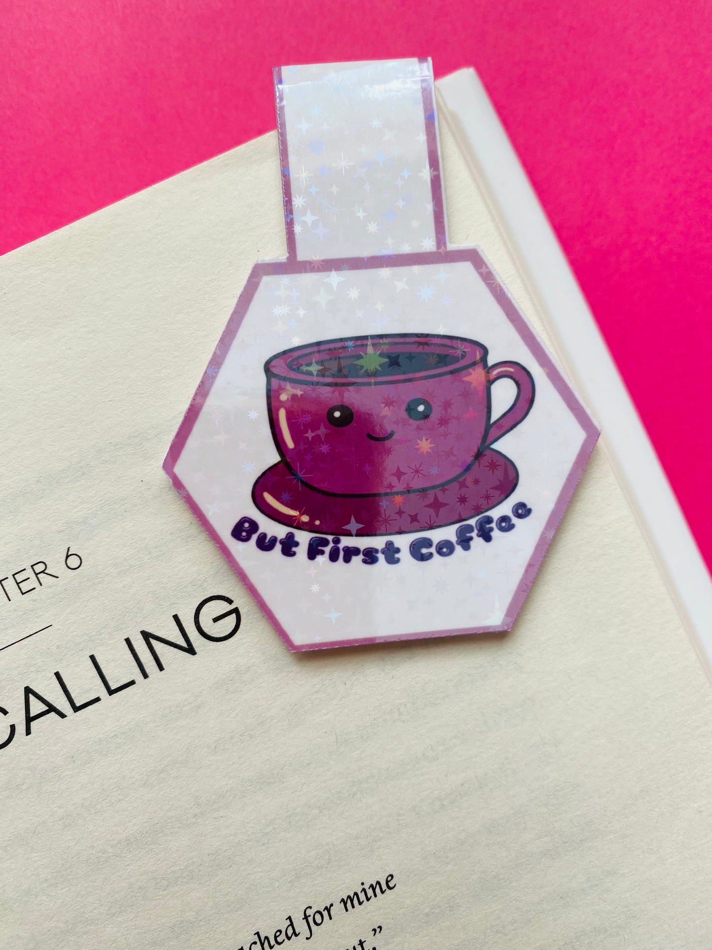 Glossy white Cardstock hexagon shaped magnetic bookmark on a Pink Background with the image of a pink cup and saucer with the text caption “But First Coffee”