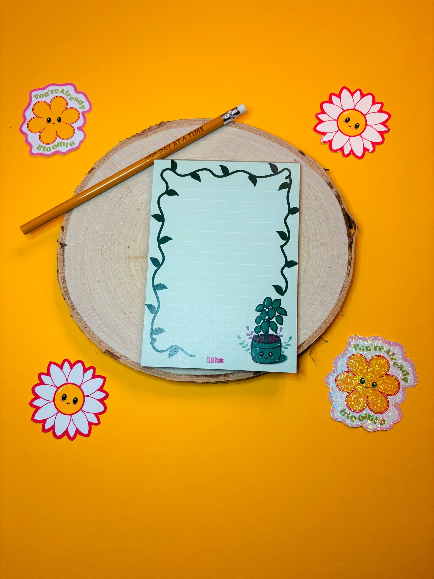 A6 sized notepad in green with the image of a Kawaii Plant surrounded by flowers and a vine border.