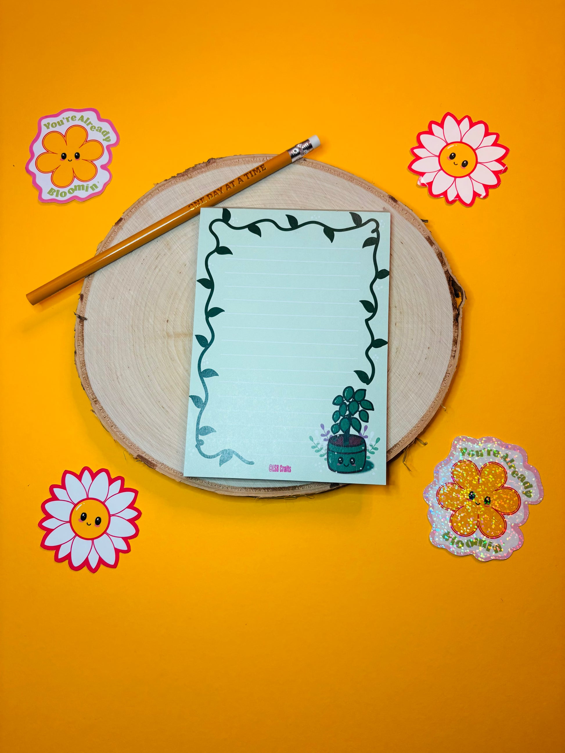 A6 sized notepad in green with the image of a Kawaii Plant surrounded by flowers and a vine border.
