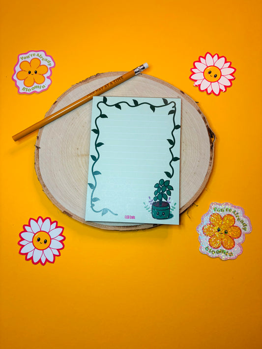 A6 sized notepad in green with the image of a Kawaii Plant surrounded by flowers and a vine border.