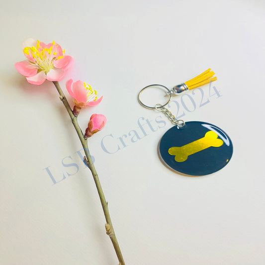 Plain Black Background (glossy) with Gold Vinyl (glossy) and Gold Tassel.

Design details on the acrylic keychain is personalised with a plain dog bone.