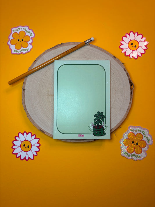 A6 sized notepad in green with the image of a Kawaii Plant surrounded by flowers and a green border